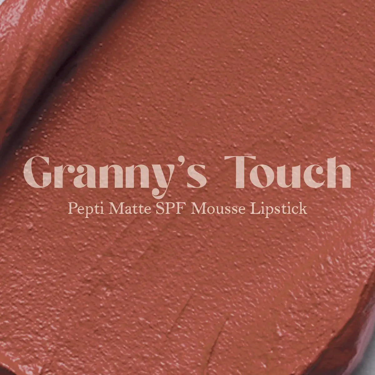 Matte lip mousse lipstick swatch, warm terracotta-red on textured surface