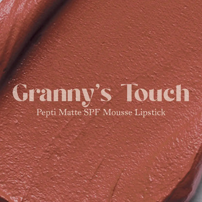 Matte lip mousse lipstick swatch, warm terracotta-red on textured surface