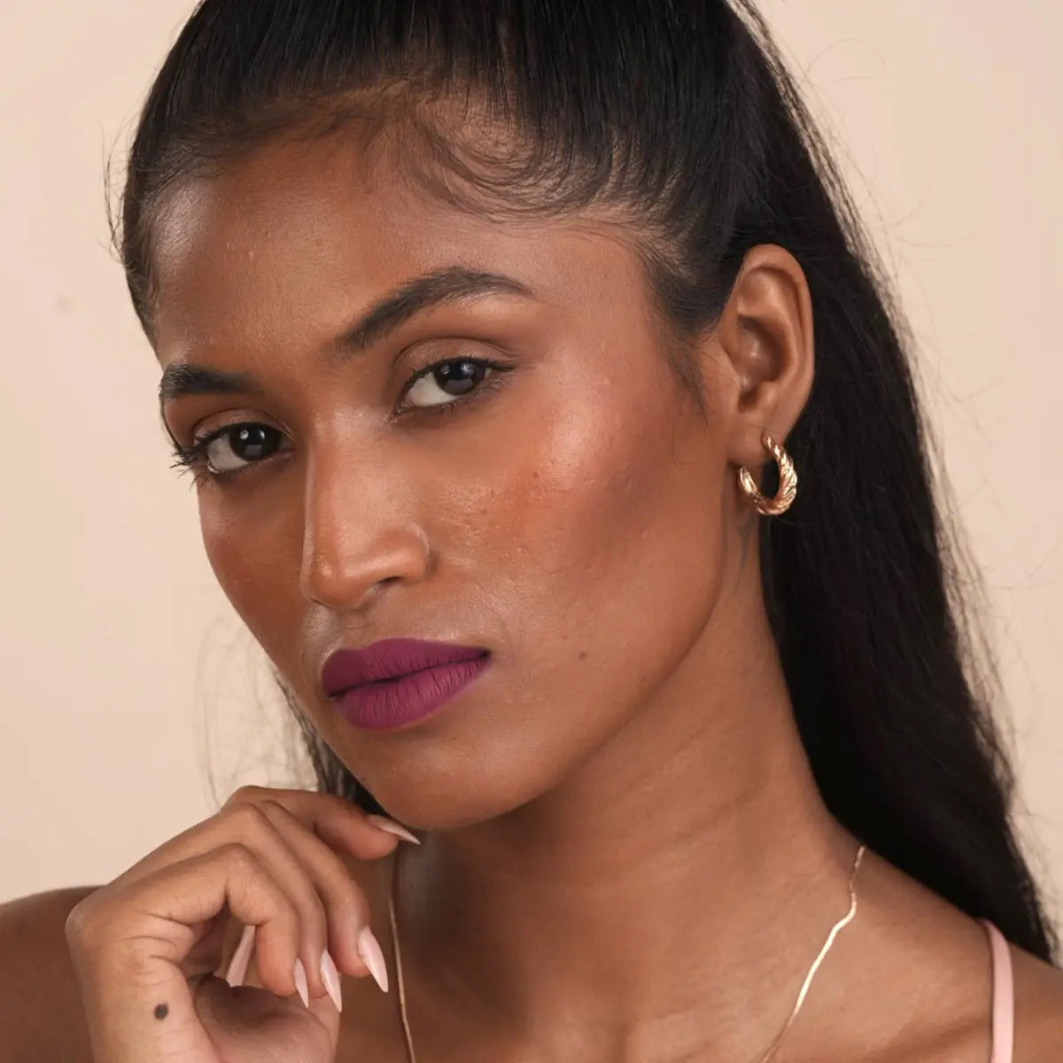 Matte plum lipstick on lips on a woman with hoop earrings and necklace