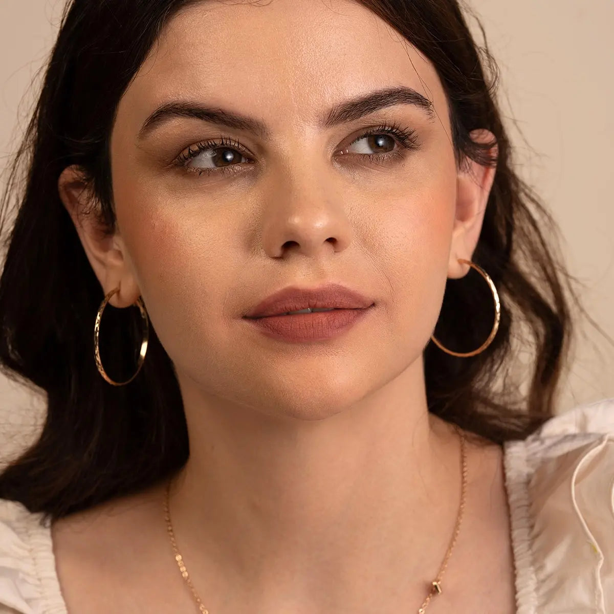 Matte berry lipstick on lips on a woman with gold hoop earrings